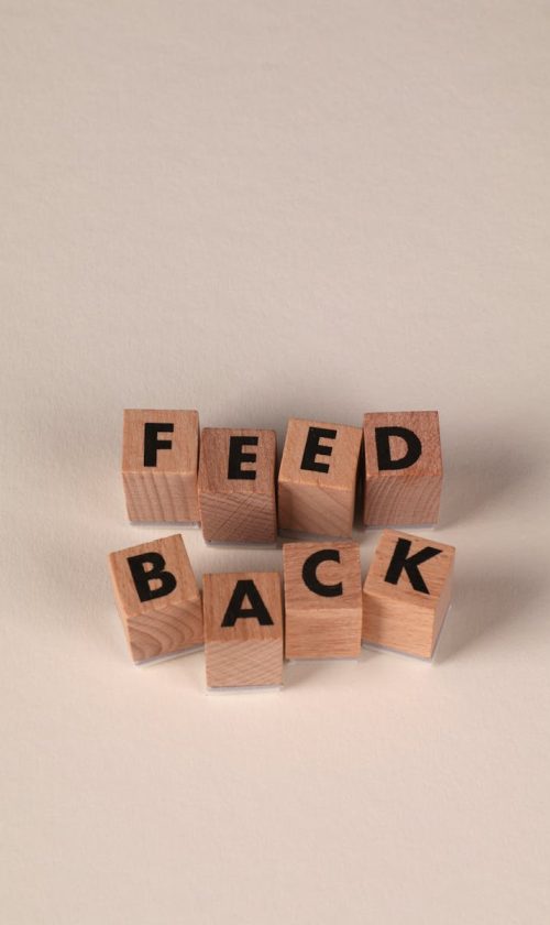 Wooden blocks forming the word 'Feedback' against a neutral beige background, conveying communication or review concept.