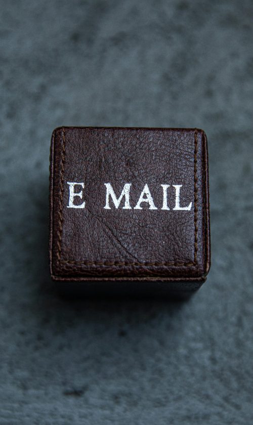 Brown leather square box with 'E MAIL' text on a gray surface, modern still life